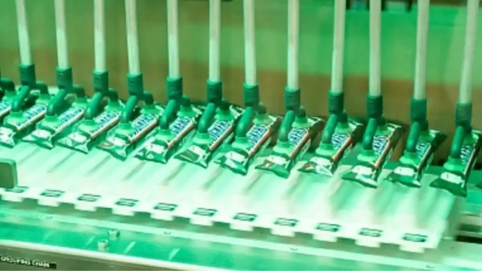 Automated packaging line placing small green pouches onto a conveyor belt for sealing or boxing.